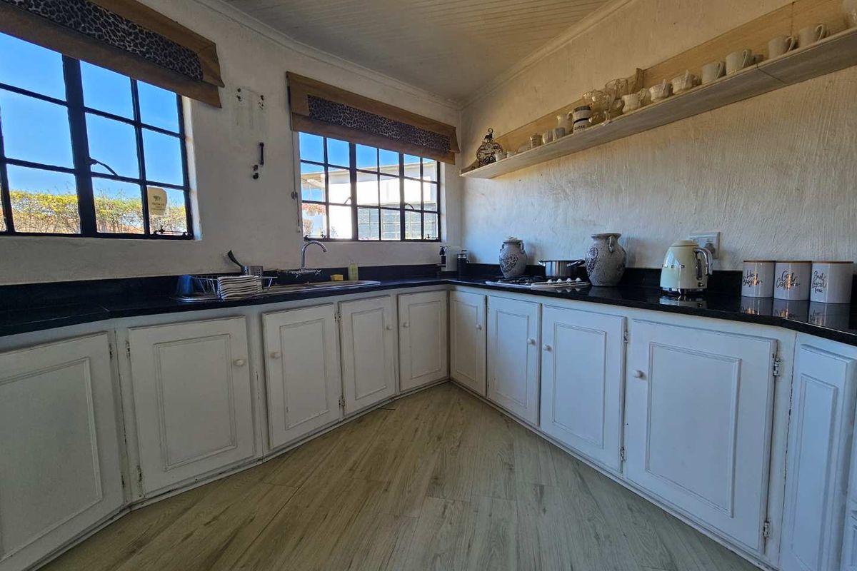 A functional kitchen featuring white cabinetry, black granite countertops, gas hob, and timber-look flooring, complemented by natural light from steel-framed windows.