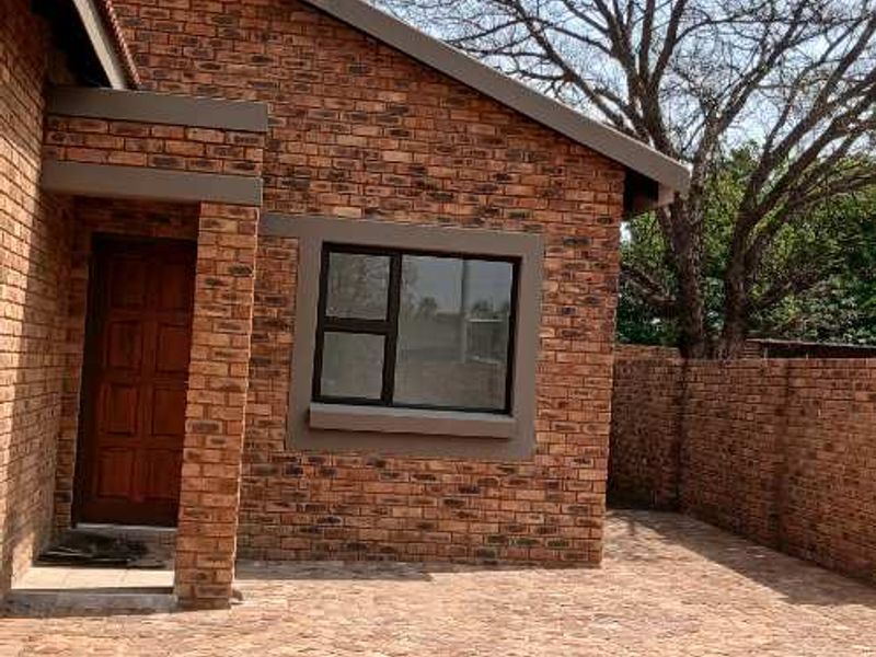 A rear view of the property featuring a face brick facade, paved patio area, and a secure timber entrance door.