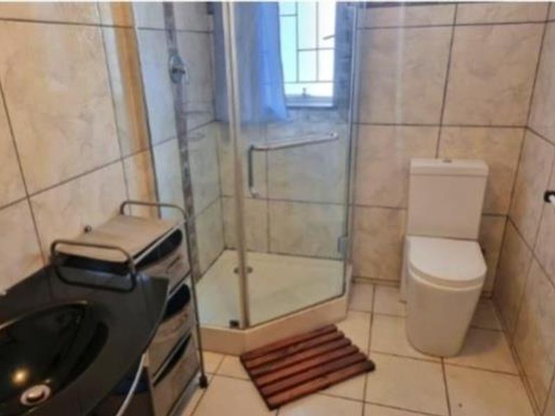 A compact bathroom featuring a corner shower enclosure, ceramic wall and floor tiles, a toilet, and a basin.