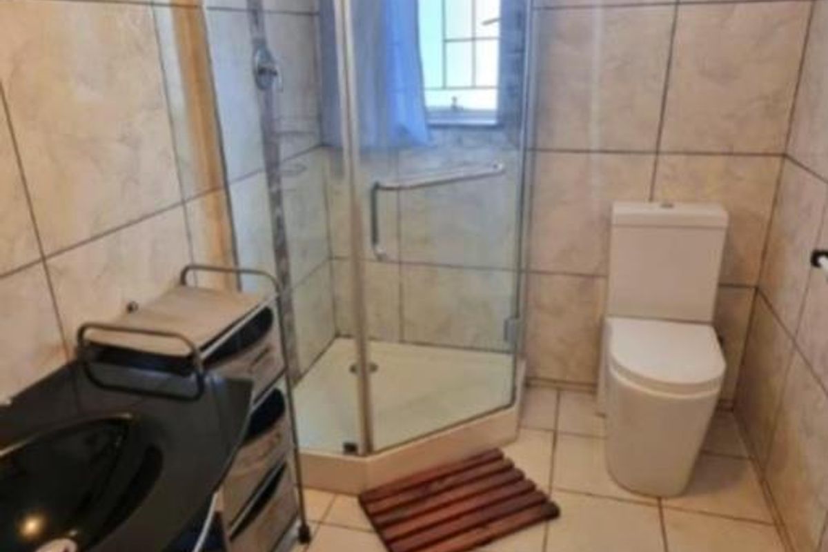A compact bathroom featuring a corner shower enclosure, ceramic wall and floor tiles, a toilet, and a basin.