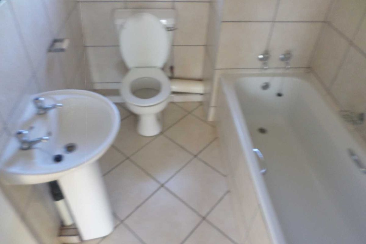 A functional bathroom featuring a pedestal basin, toilet, and bathtub with tiled walls and flooring.