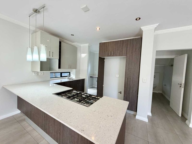 Modern kitchen featuring two-tone cabinetry, stone countertops, integrated gas cooktop, and tiled flooring, with an adjacent scullery area.