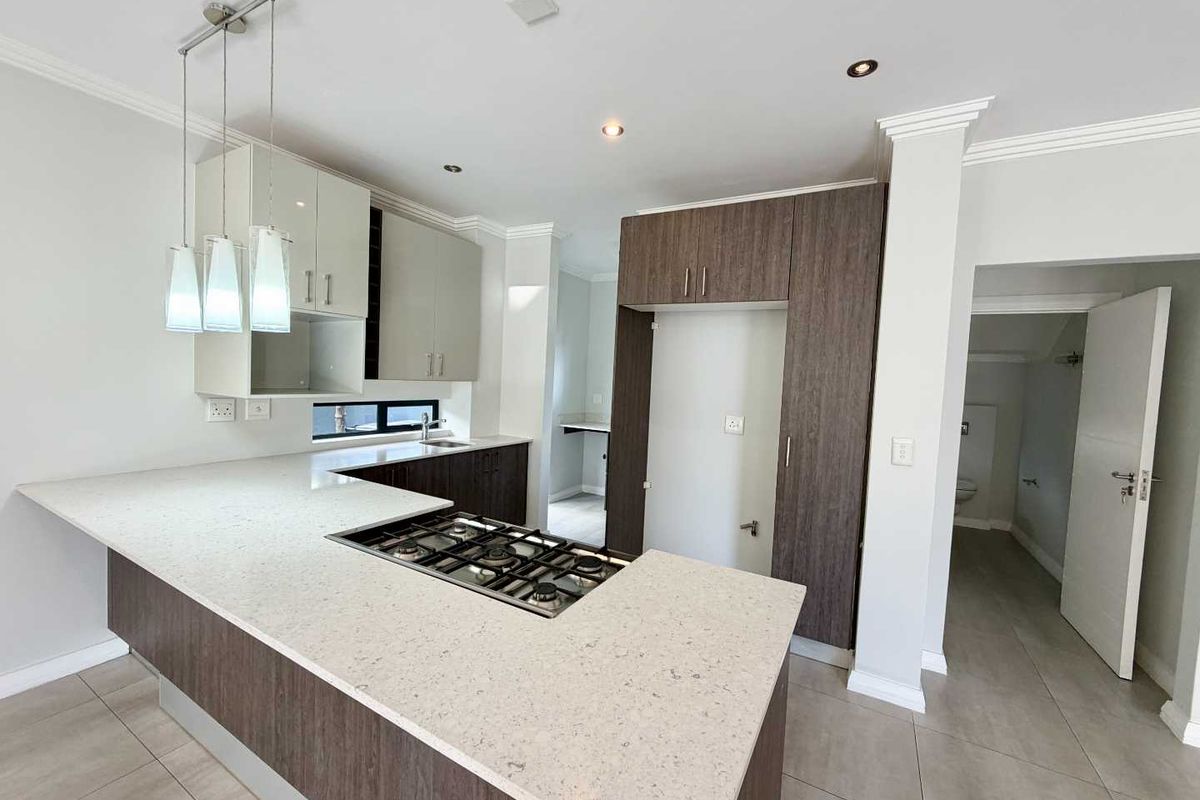 Modern kitchen featuring two-tone cabinetry, stone countertops, integrated gas cooktop, and tiled flooring, with an adjacent scullery area.