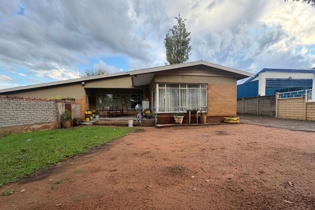 Rear view of the house featuring a brick facade, large windows, and a covered patio area overlooking an unpaved yard.