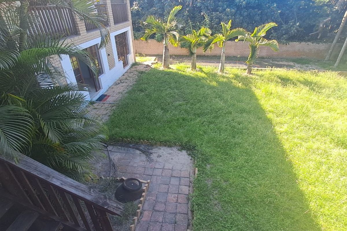 A rear view of the property featuring a brick facade, a wooden staircase leading to the garden, and a paved patio area.