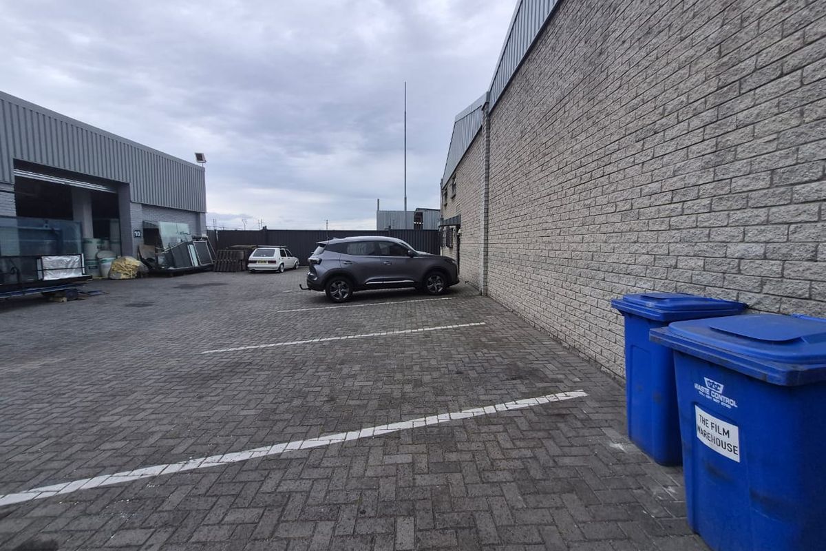 Rear industrial yard area featuring paved parking space, brick wall construction, and access to a warehouse unit with a roller door.