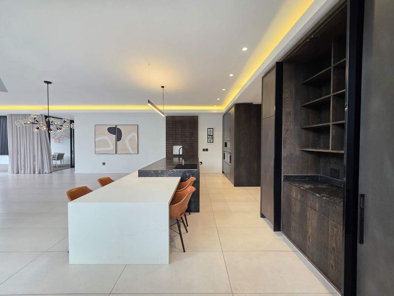 Modern open-plan living area featuring a sleek kitchen with a large island, stone countertops, custom dark wood cabinetry, and sophisticated recessed lighting.