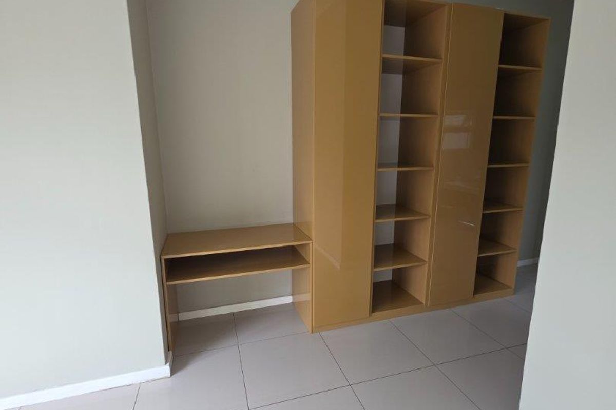 A clean, empty bedroom featuring neutral wall tones, modern tiled flooring, and integrated built-in storage cabinetry with an attached desk unit.