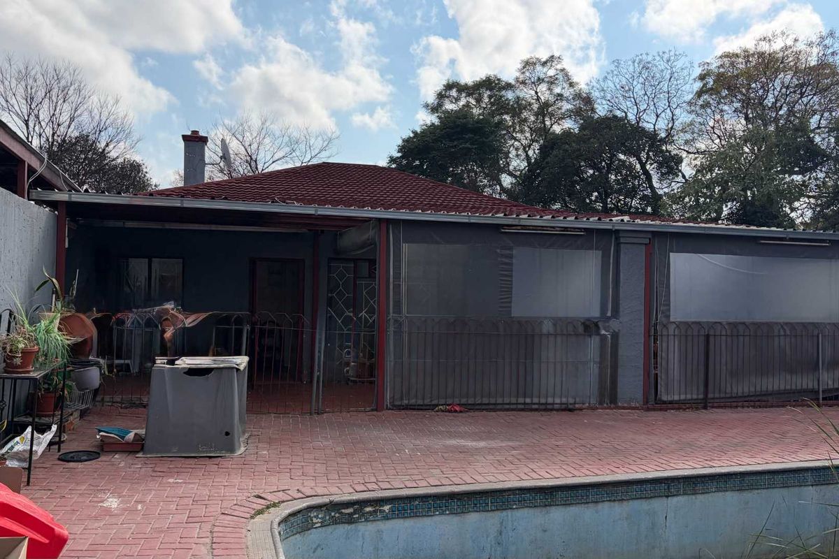 Rear exterior view featuring a covered patio area, brick paving, and an in-ground swimming pool with visible wear.