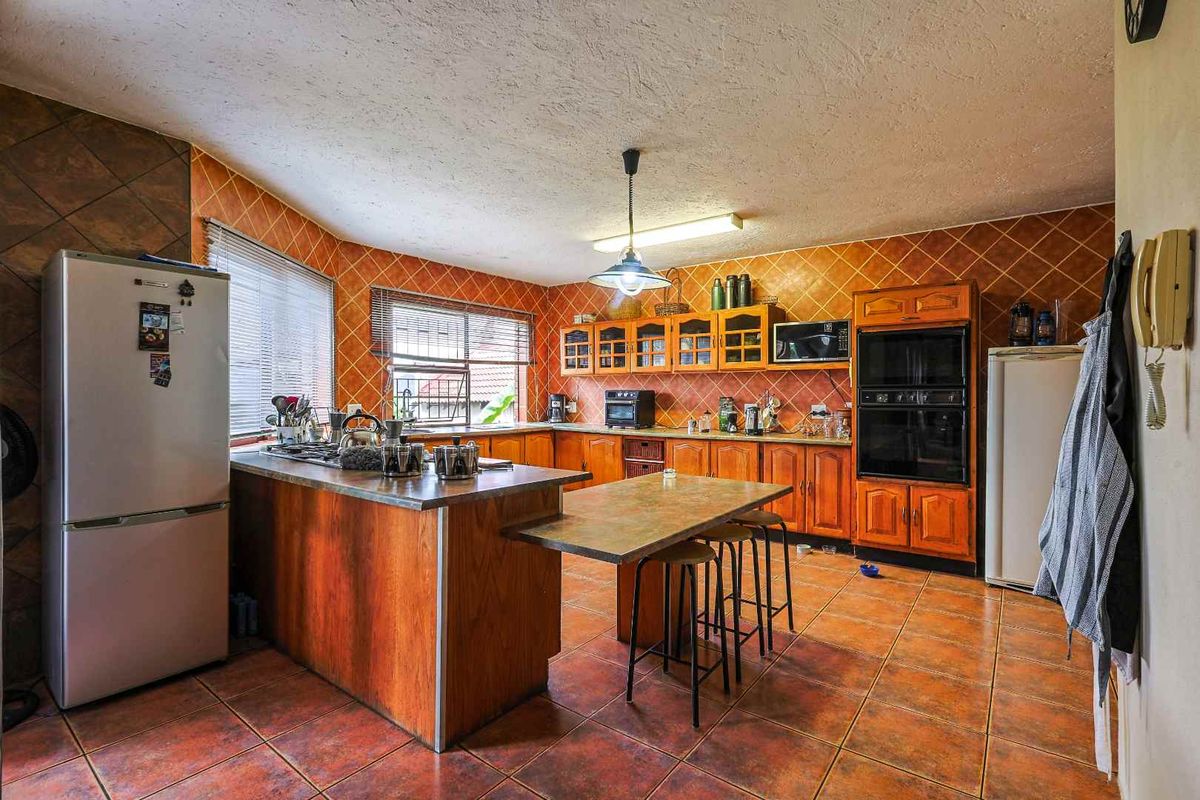 Spacious kitchen featuring wooden cabinetry, integrated oven, built-in hob, and tiled flooring with a central breakfast bar island.