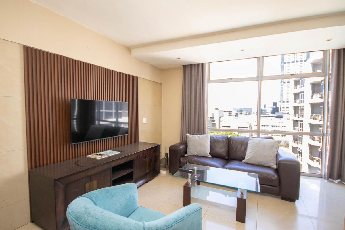 A modern living room featuring a decorative slatted timber wall, large windows with city views, and recessed ceiling lighting.