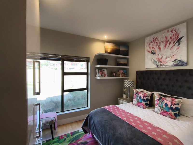 A well-maintained bedroom featuring laminate flooring, built-in wall shelving, and a large window with aluminium frames, providing a bright and comfortable living space.