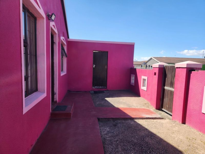Rear exterior view of the property featuring a concrete pathway, wooden gate, and painted exterior walls.