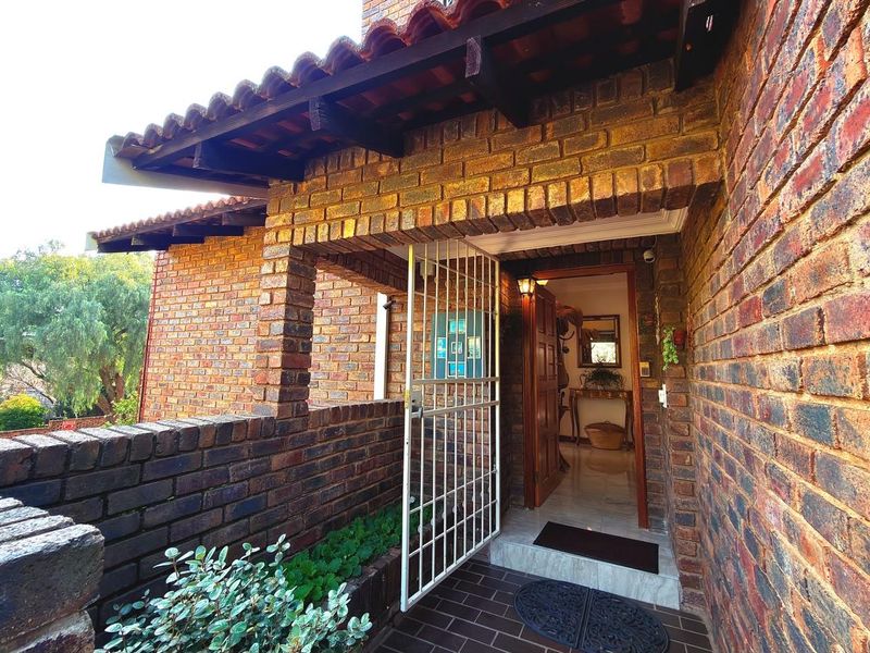 A welcoming entrance featuring a classic face brick facade, a secure metal gate, and a covered porch leading into the home.
