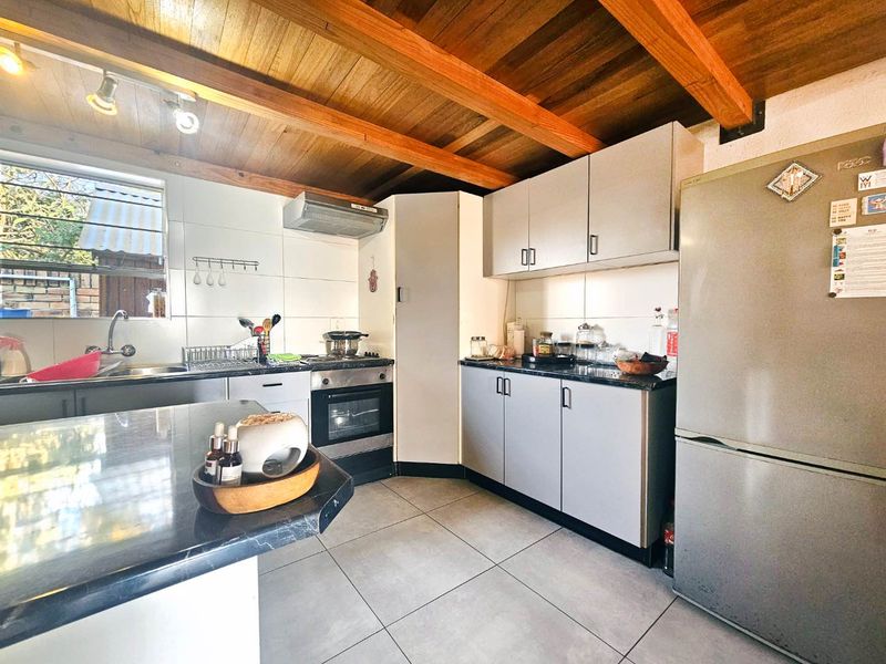 Functional kitchen featuring built-in cabinetry, integrated oven and hob, double sink, and distinctive exposed timber ceiling beams.