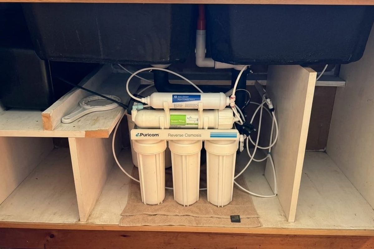 Under-sink cabinet space featuring a Puricom reverse osmosis water filtration system with integrated plumbing connections.