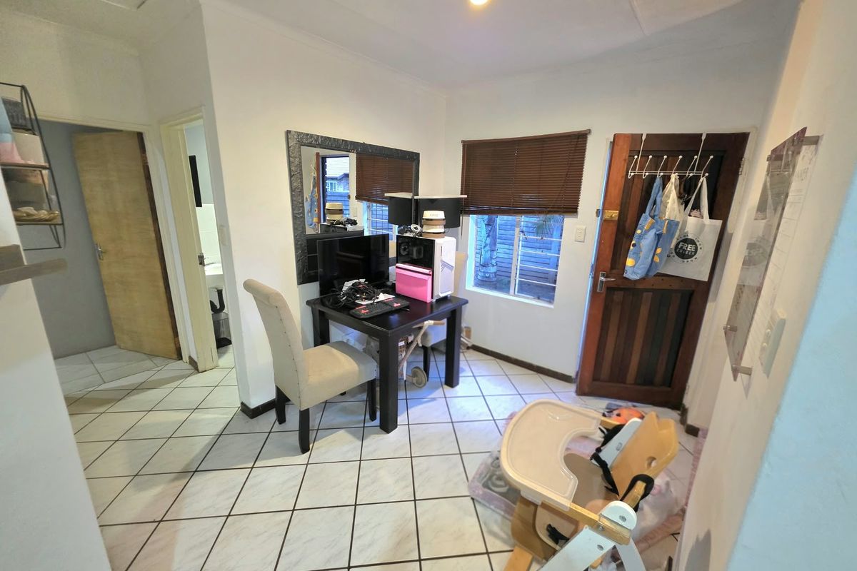 A small living area featuring tiled flooring, a timber entrance door, and venetian blinds, currently utilized as a multi-purpose space.
