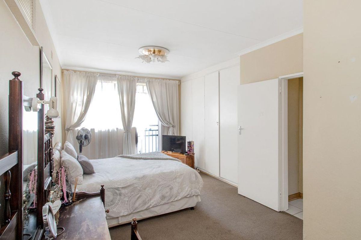 A bedroom featuring built-in cupboards, carpeted flooring, and access to a balcony through sliding glass doors.