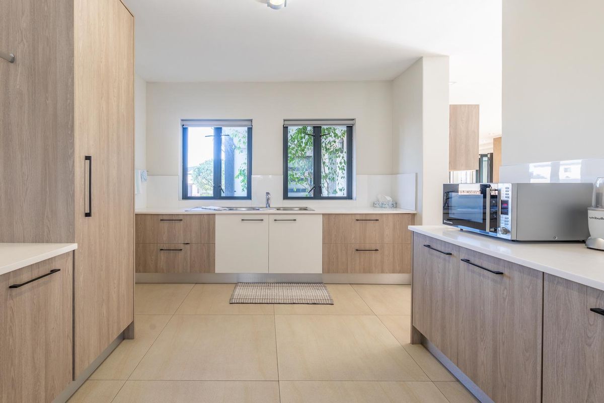 Modern kitchen featuring light wood-tone cabinetry, stone countertops, dual windows, and tiled flooring, offering a clean and functional workspace.