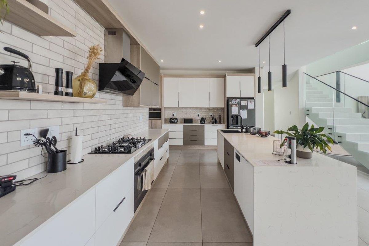 Modern kitchen featuring a large central island, stone countertops, gas hob, built-in oven, extractor fan, and sleek cabinetry with integrated lighting.