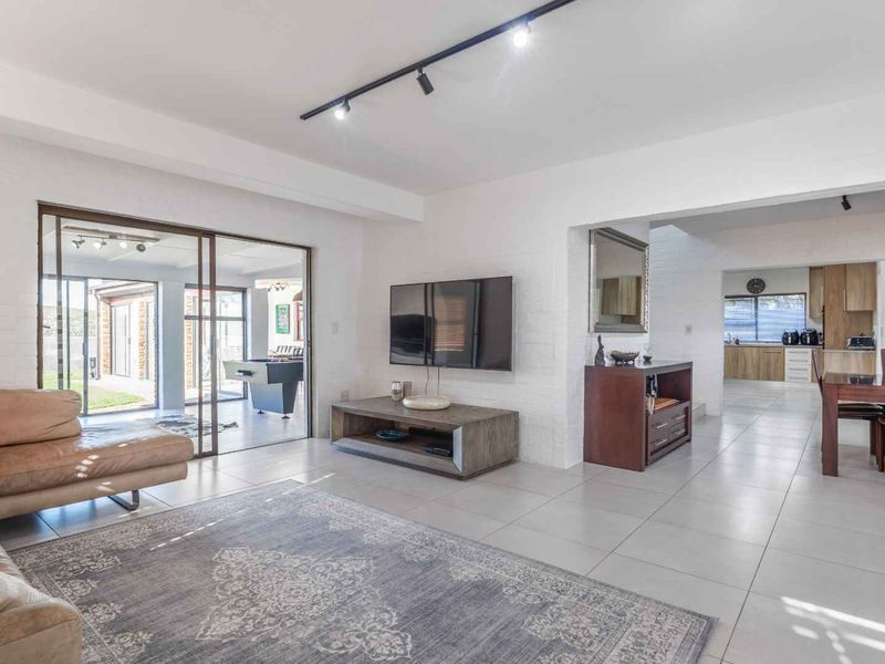 Spacious open-plan living and dining area featuring modern track lighting, neutral tiled flooring, and large sliding doors leading to an outdoor patio.