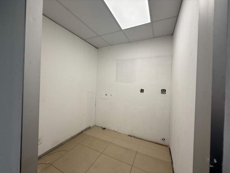 A vacant office space featuring a suspended ceiling, recessed lighting, and tiled flooring, currently requiring cosmetic wall repairs and finishing.