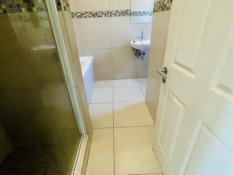 A functional bathroom featuring a shower enclosure, bathtub, and wall-mounted basin with neutral tiled finishes and a decorative mosaic border.