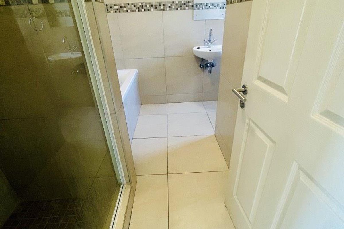 A functional bathroom featuring a shower enclosure, bathtub, and wall-mounted basin with neutral tiled finishes and a decorative mosaic border.