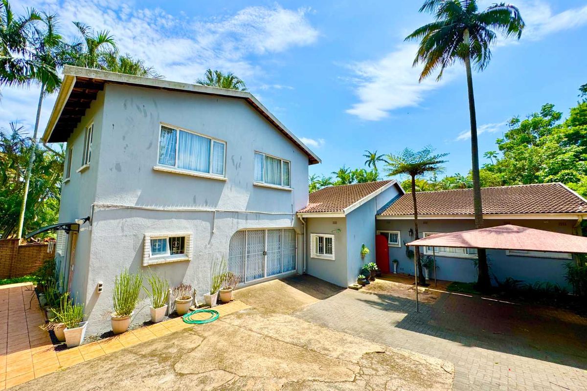 Rear view of the property featuring a paved courtyard, covered patio area, and established garden surroundings.