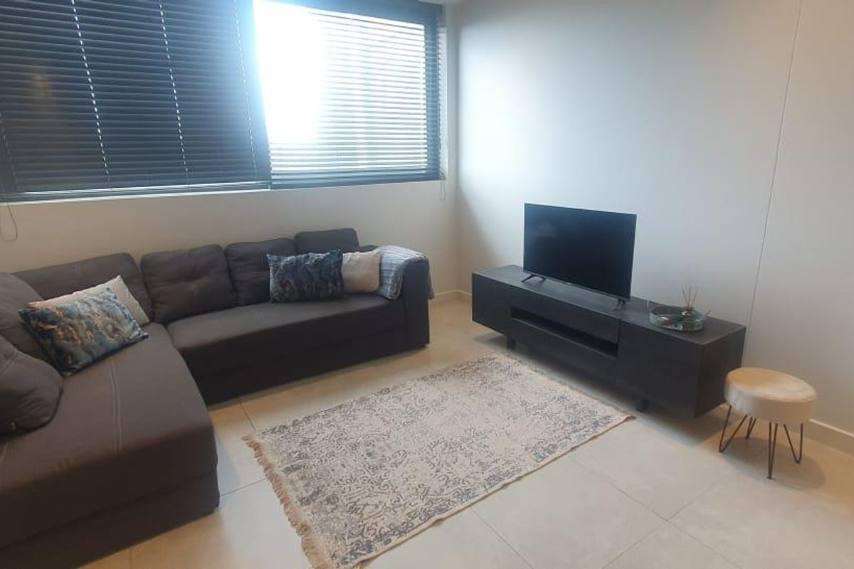 A modern living room featuring neutral tiled flooring and large windows fitted with venetian blinds, offering a clean and functional space.