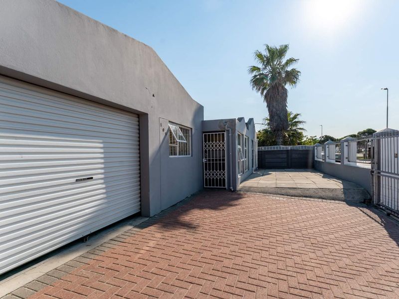 Front exterior view featuring a paved driveway, roller garage door, and secure perimeter fencing with security gates.