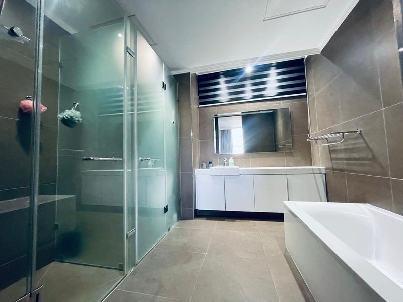 Modern bathroom featuring a glass-enclosed shower, a built-in vanity with storage, a bathtub, and neutral floor-to-ceiling tiling.