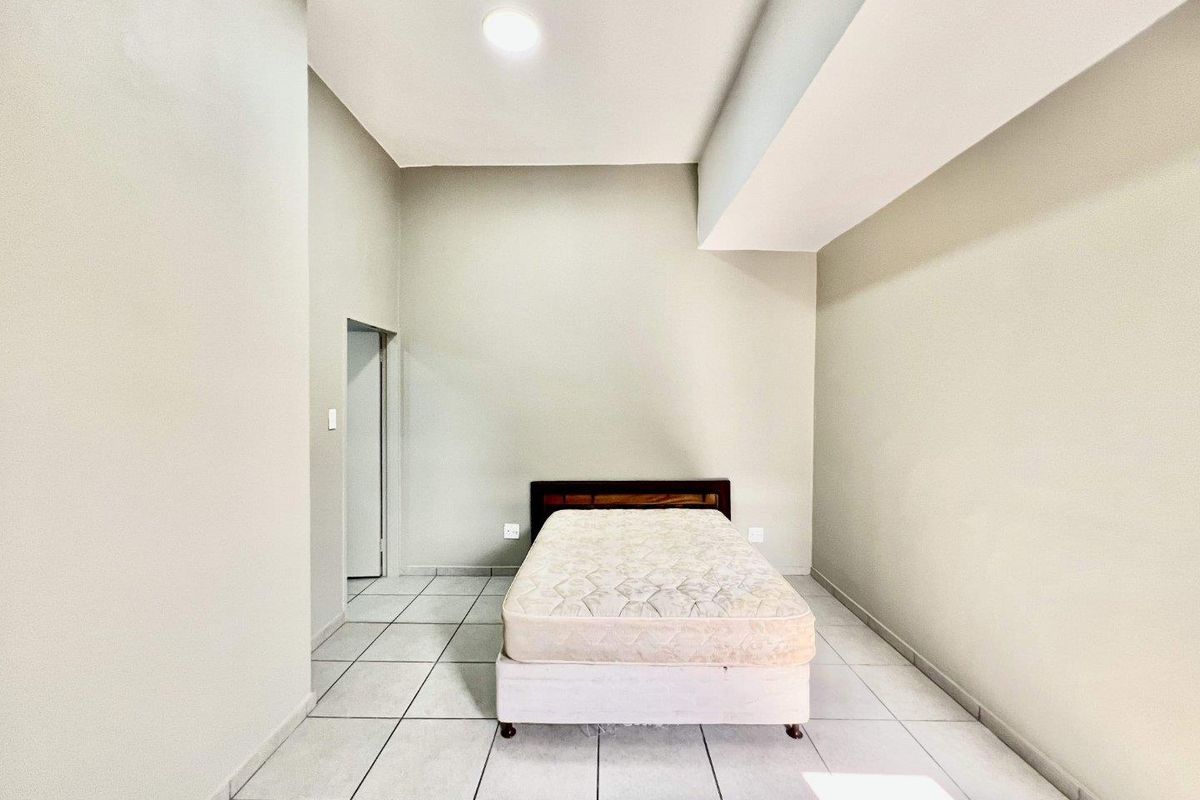 A simple bedroom featuring neutral walls, tiled flooring, and a recessed ceiling detail, providing a clean and functional living space.