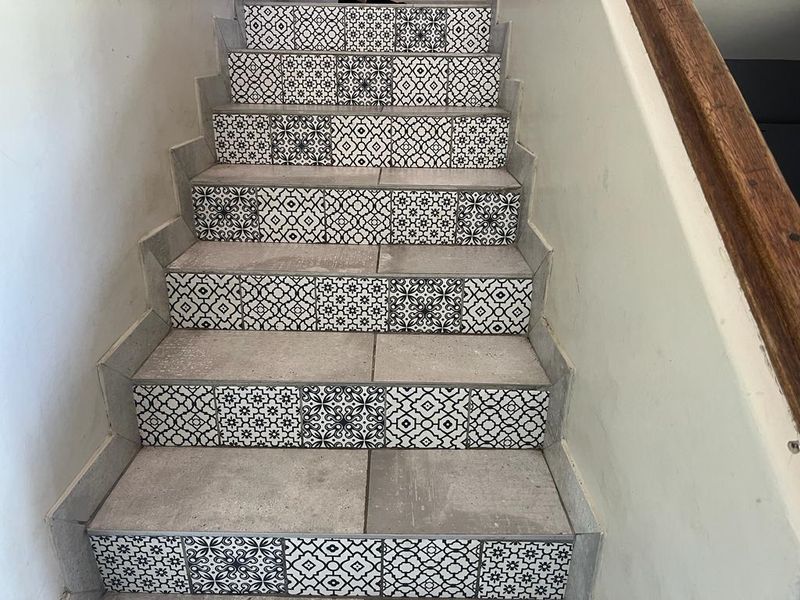 A staircase featuring decorative patterned tile risers and concrete-look treads, complemented by a simple wooden handrail.