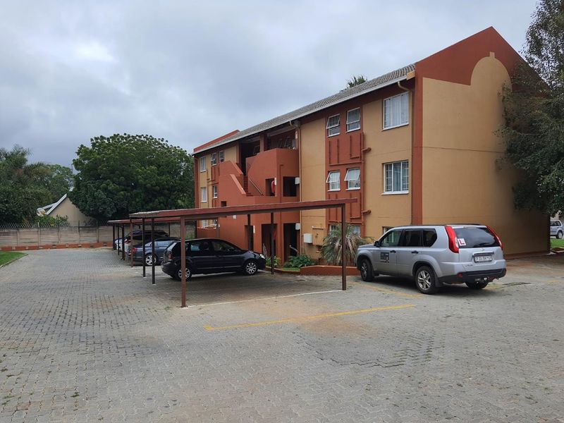 Exterior view of a multi-story apartment building featuring a paved parking area with covered carports and external stair access.