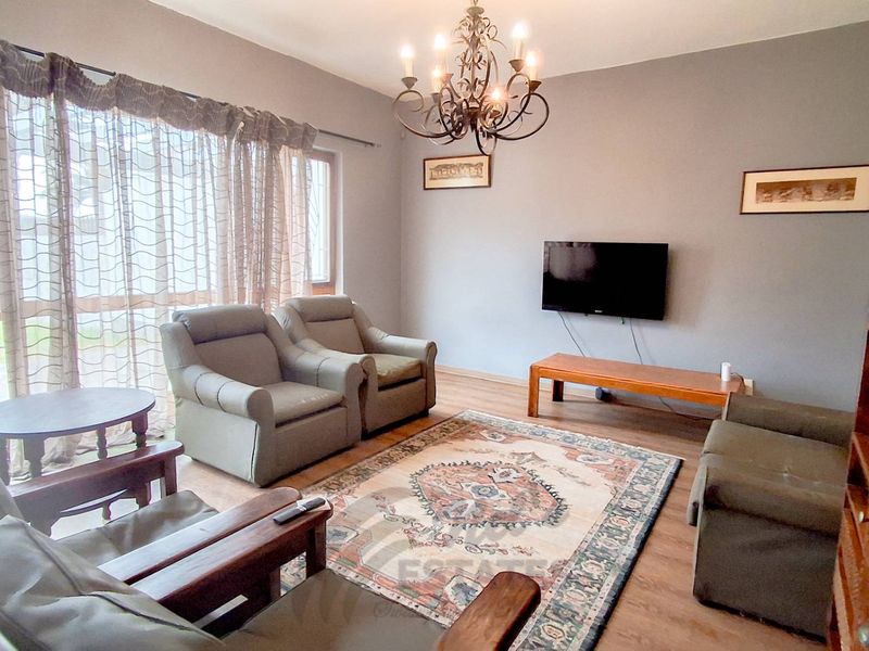 A comfortable living room featuring laminate flooring, a decorative wrought iron chandelier, and large windows allowing for natural light.