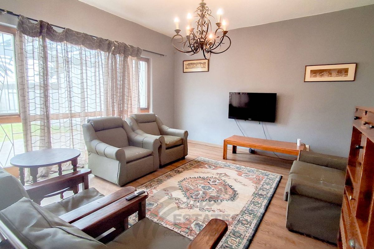 A comfortable living room featuring laminate flooring, a decorative wrought iron chandelier, and large windows allowing for natural light.