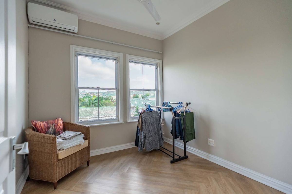A bright bedroom featuring herringbone wood flooring, a split-system air conditioner, and large sash windows offering an elevated view.