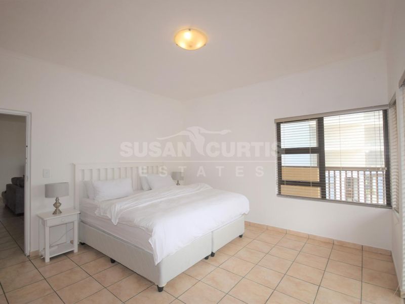 A bright bedroom featuring neutral tiled flooring, aluminium window frames with fitted blinds, and a central ceiling light fixture.