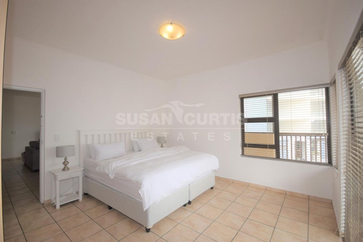 A bright bedroom featuring neutral tiled flooring, aluminium window frames with fitted blinds, and a central ceiling light fixture.