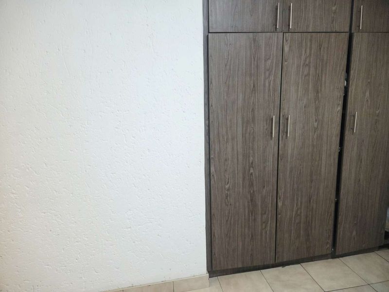 A bedroom interior featuring modern wood-grain built-in cupboards and neutral tiled flooring.