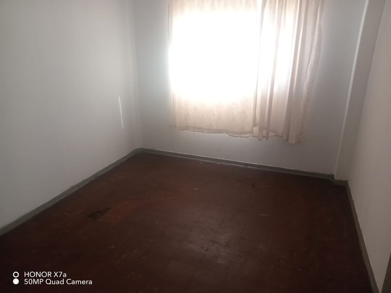 An empty bedroom featuring tiled flooring and a window with curtains, requiring cosmetic updates to improve the overall condition.