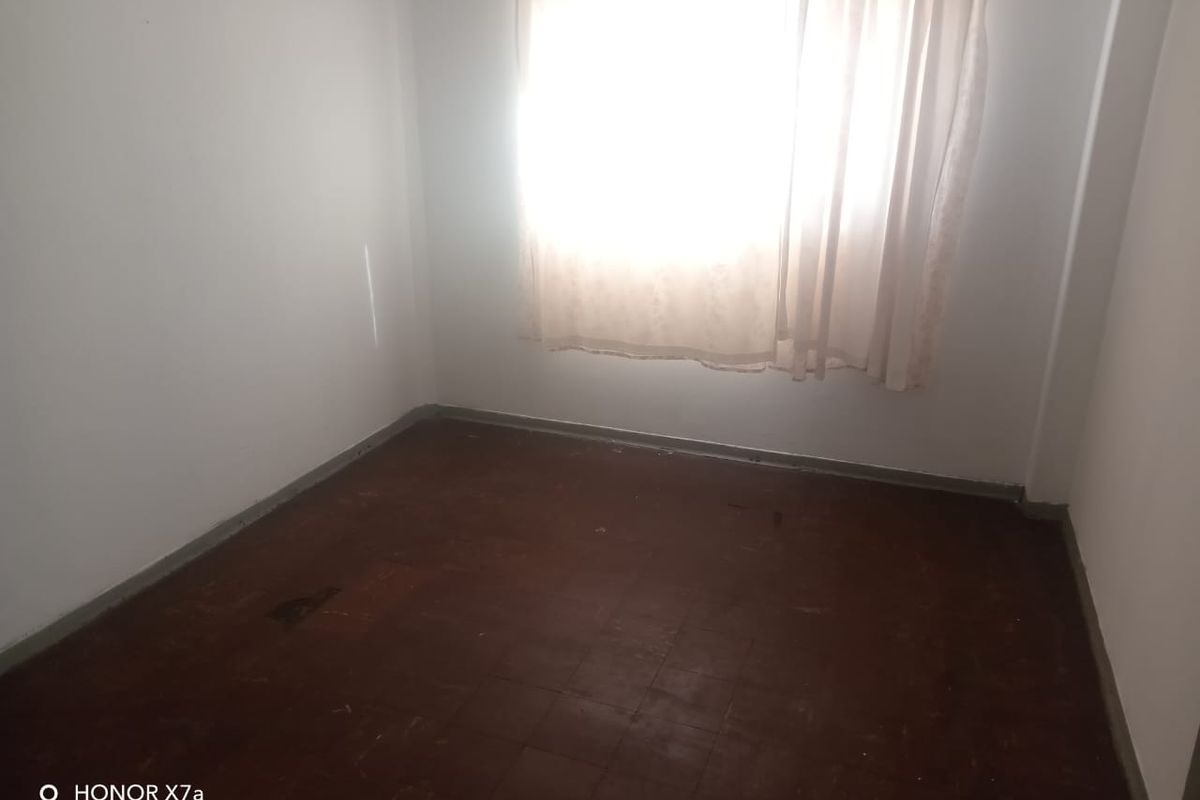 An empty bedroom featuring tiled flooring and a window with curtains, requiring cosmetic updates to improve the overall condition.