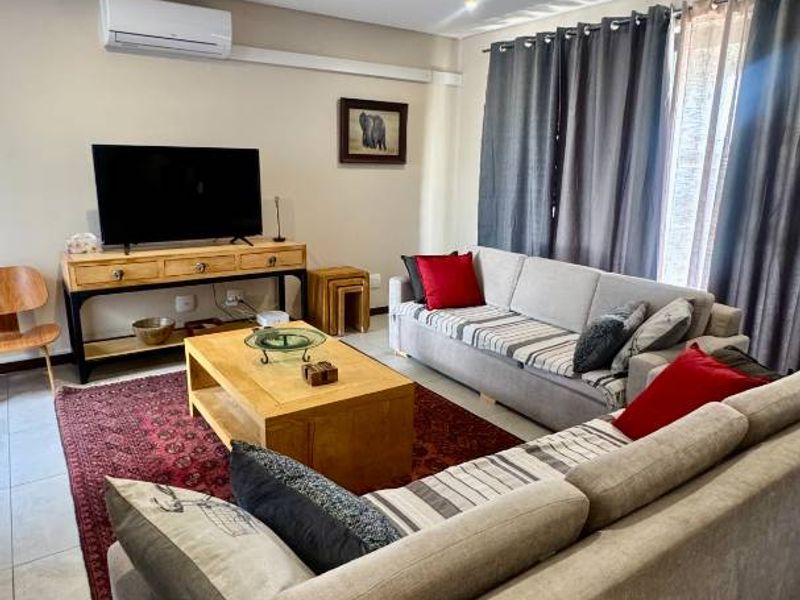 A comfortable living room featuring tiled flooring, recessed downlighting, and a wall-mounted split-system air conditioning unit.