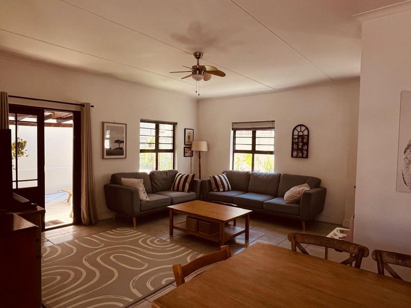 A comfortable living room featuring tiled flooring, a ceiling fan, and large windows, with direct access to an outdoor patio area.