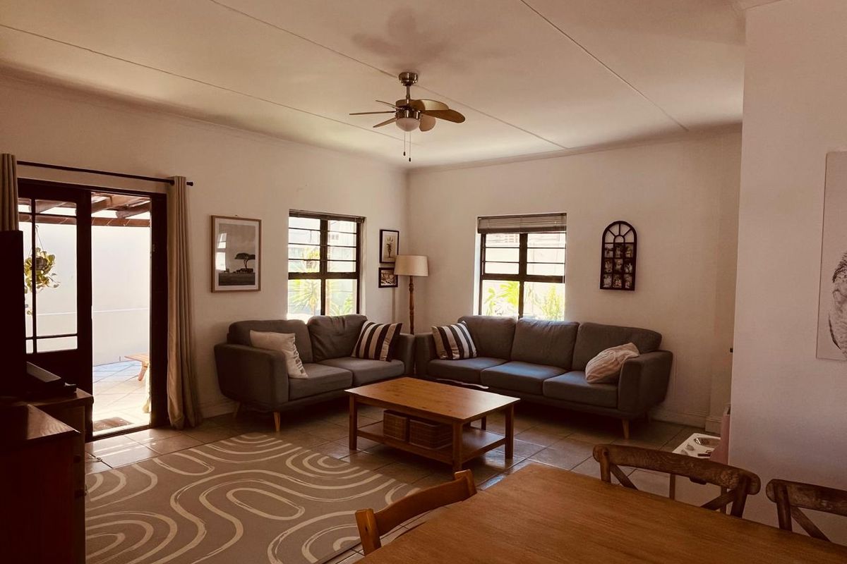 A comfortable living room featuring tiled flooring, a ceiling fan, and large windows, with direct access to an outdoor patio area.