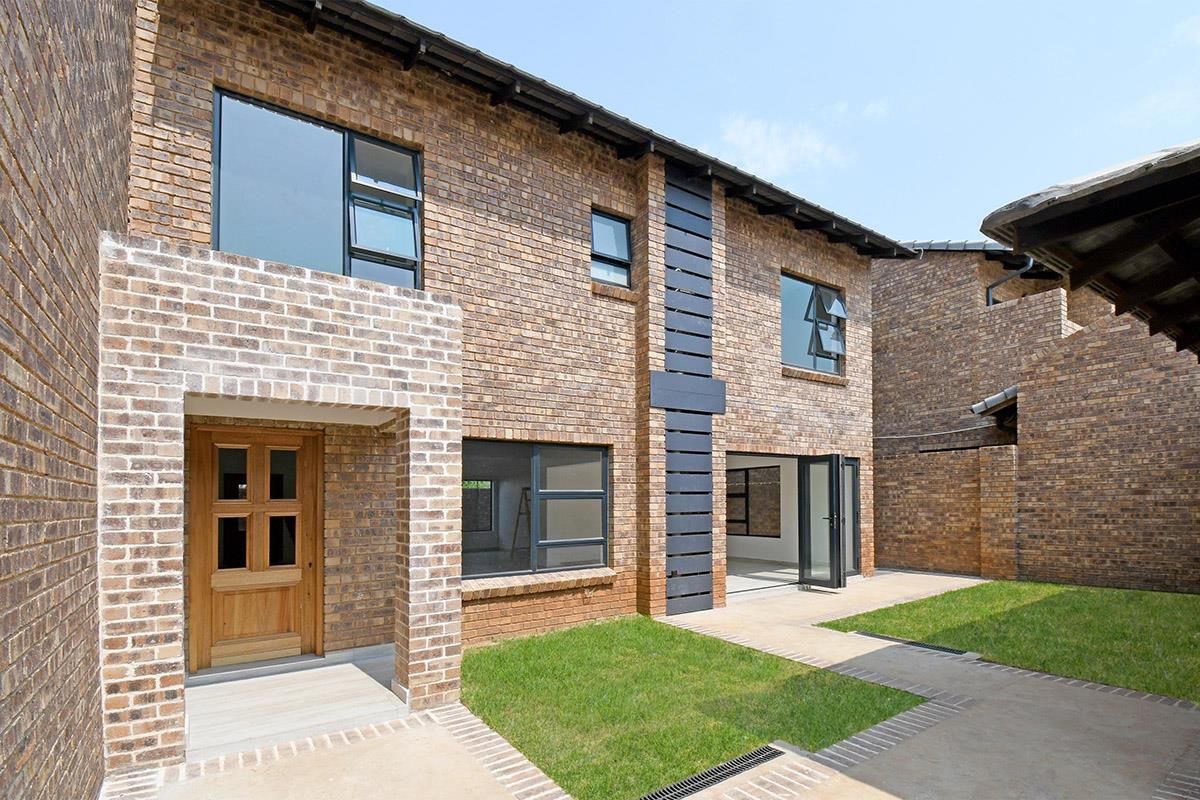 A view of the rear exterior of a modern brick cluster home, featuring a small garden, paved walkway, and large windows.