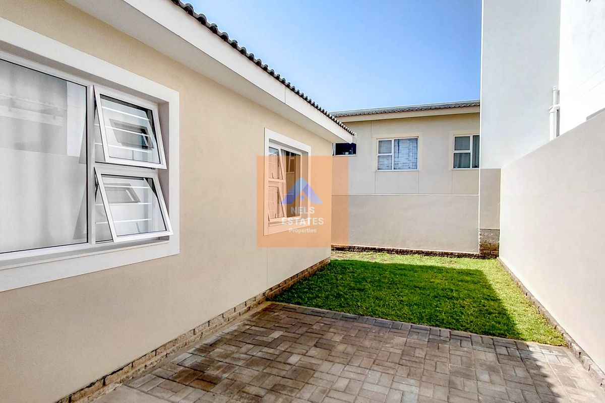 A neat rear exterior view featuring a paved patio area, a small lawn, and boundary walls, providing a private outdoor space.