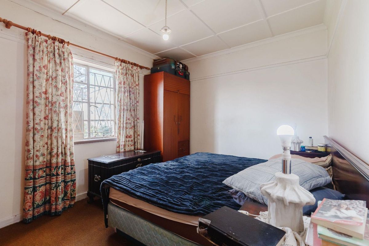 A bedroom featuring a built-in wardrobe, security bars on the window, and a tiled ceiling, offering a functional space with potential for modernization.