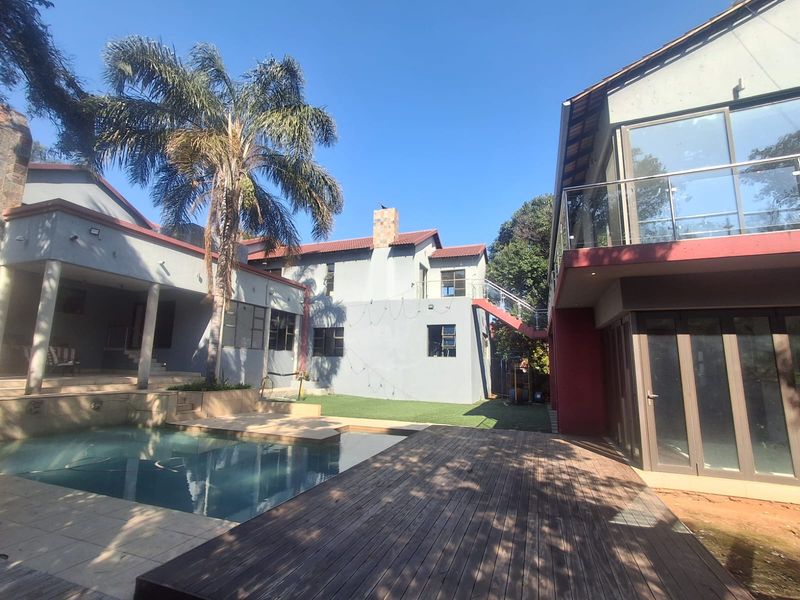Spacious rear exterior featuring a swimming pool, timber decking, and a multi-level home structure with balconies and glass balustrades.